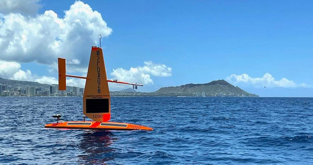 An autonomous Saildrone Explorer vessel navigating ocean waves in the open Pacific under cloudy skies.