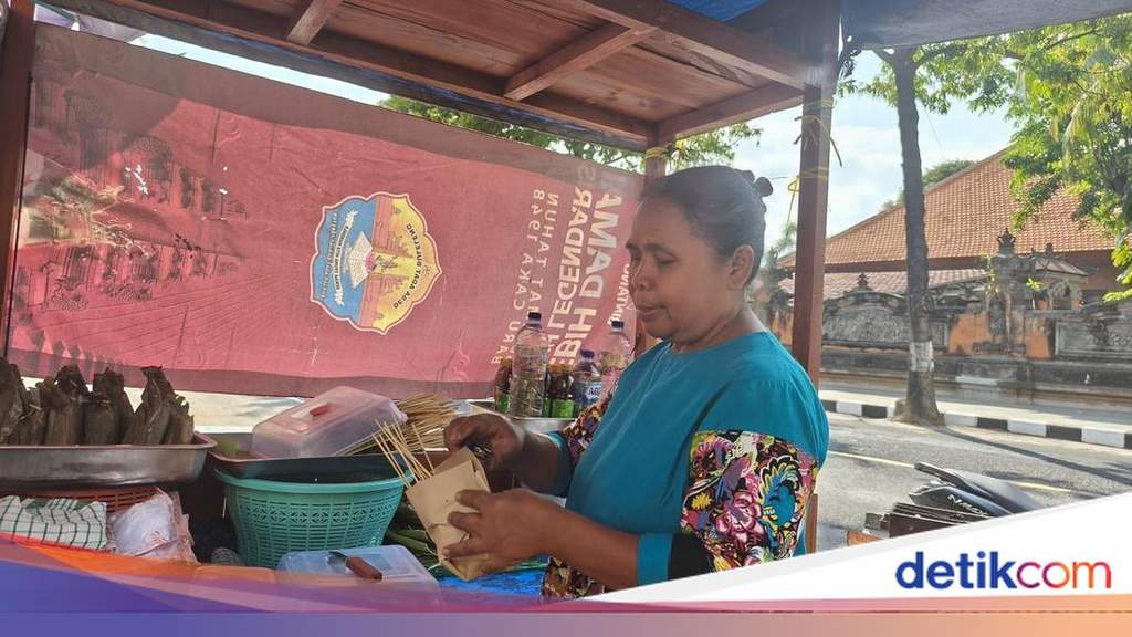 A local female satay vendor cheerfully serving food to customers at her bustling makeshift stall located within the newly revitalized public area in Singaraja, Bali.