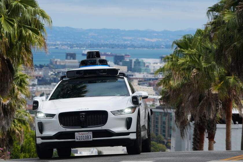 A Waymo autonomous vehicle driving down a street in San Francisco with its sensor dome active on top during a clear day.